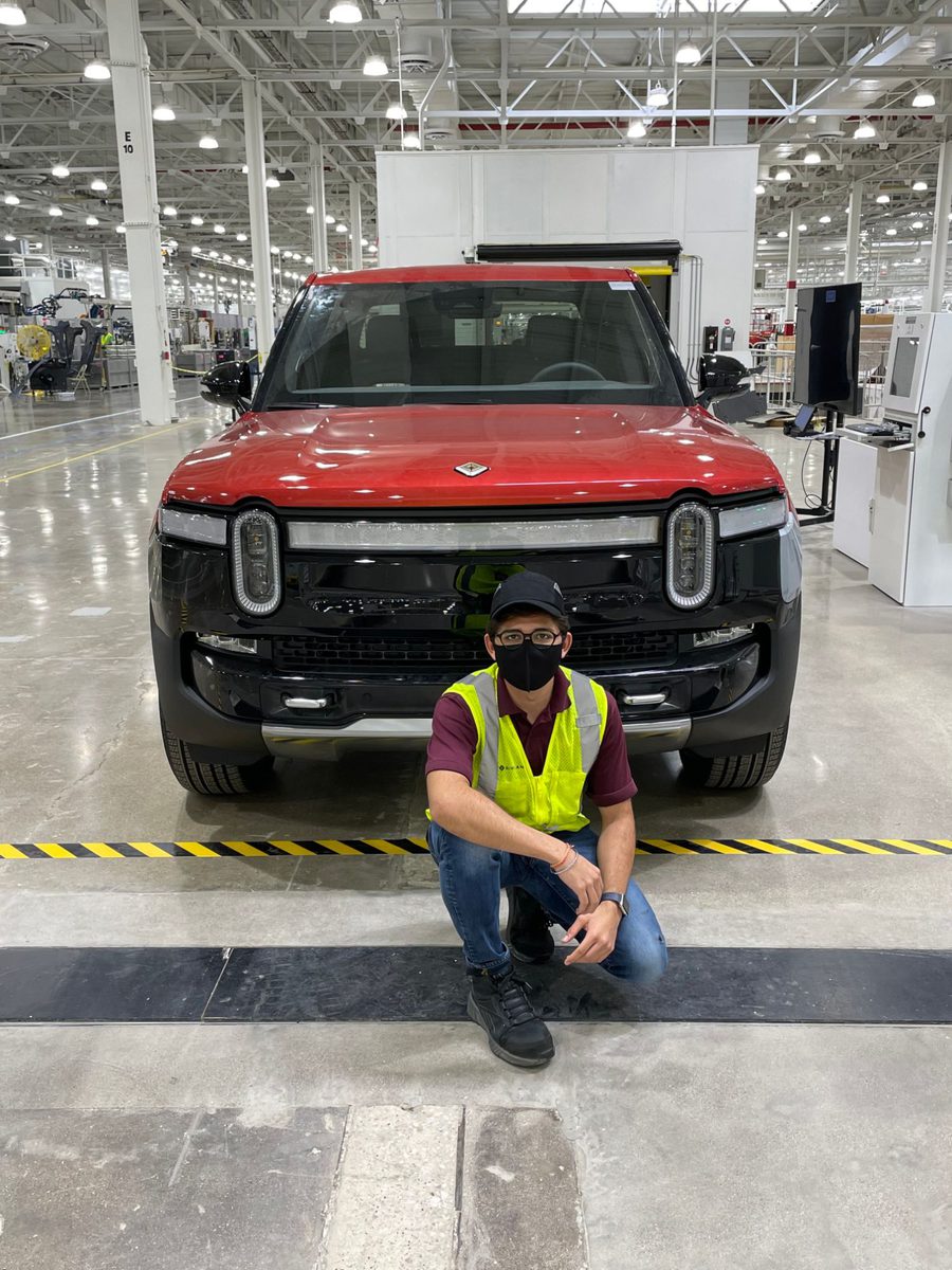 Pratik kneeling in front of a pre-production pickup truck on a factory floor