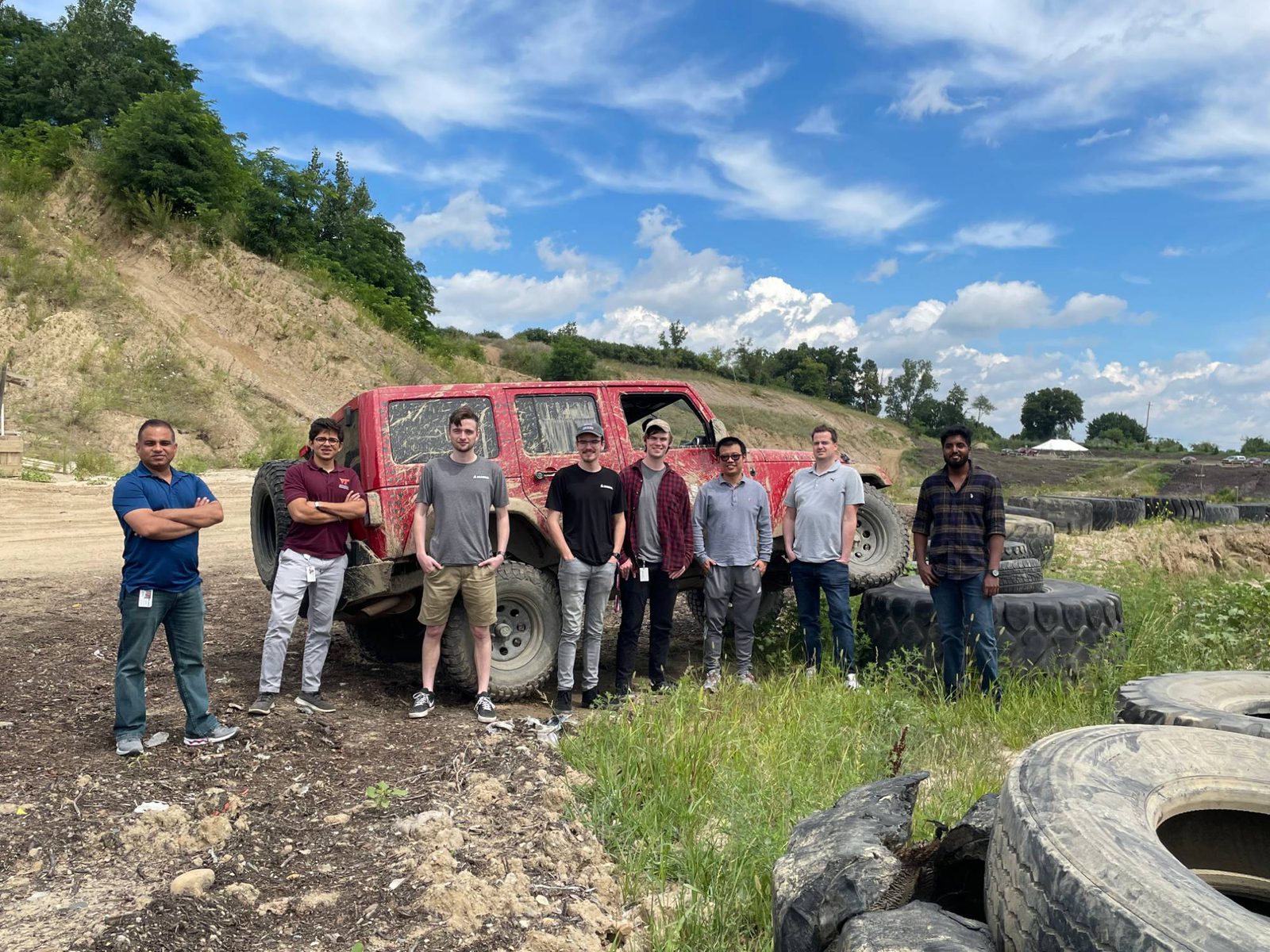 Pratik with the vehicle testing team beside a mud-covered Jeep at an off-road test site
